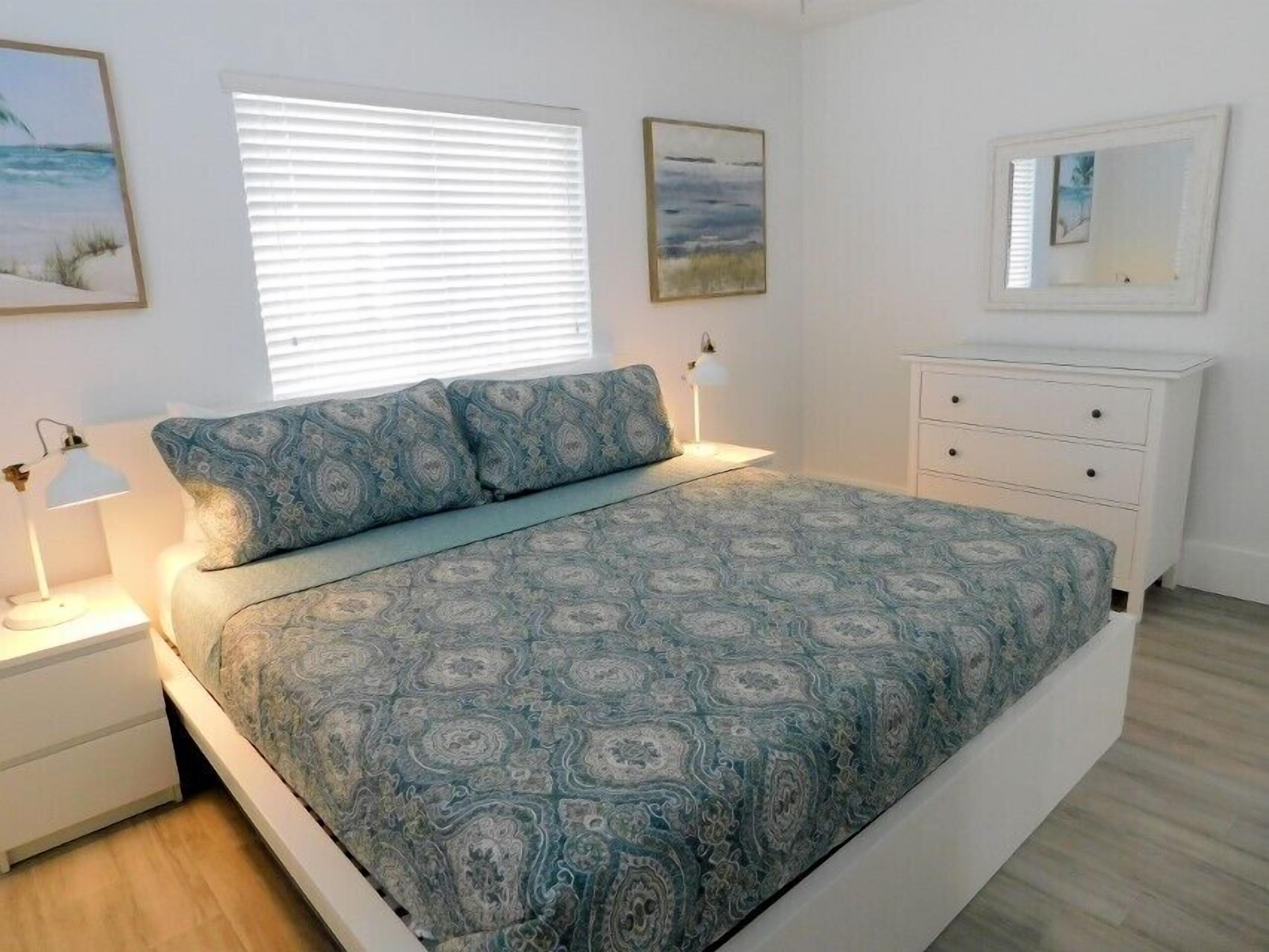 A bedroom with a bed, bedside lamps, a dresser, and artwork on the walls.