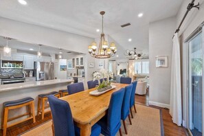 A spacious dining area with a wooden table and blue chairs, a kitchen with modern appliances, and a chandelier.