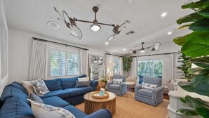 Una sala de estar con un sofá azul, sillones a rayas, una mesa de centro redonda y ventiladores de techo.