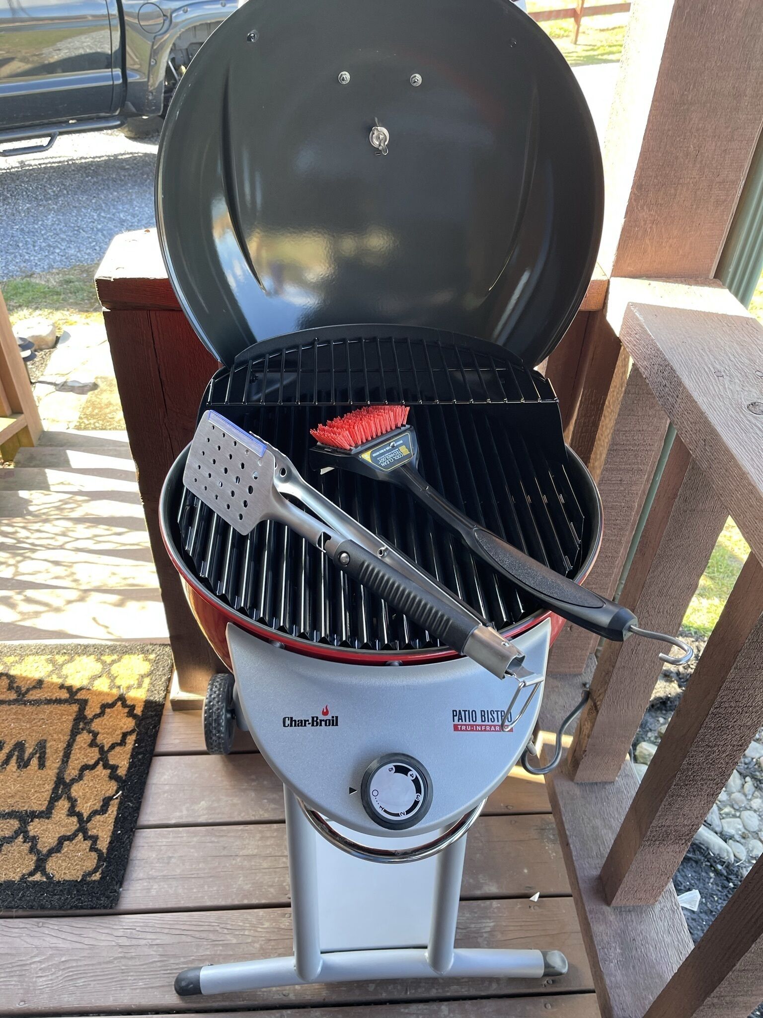 Una griglia da patio Char-Broil con coperchio nero, una spazzola rossa e pinze metalliche.