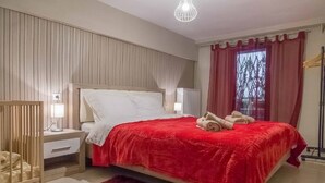 Une chambre à coucher avec un grand lit, une table de chevet, un berceau et une fenêtre avec des rideaux.