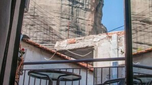 Un balcon avec des chaises et une table en métal, donnant sur une falaise rocheuse et un bâtiment doté d’un toit en tuiles.