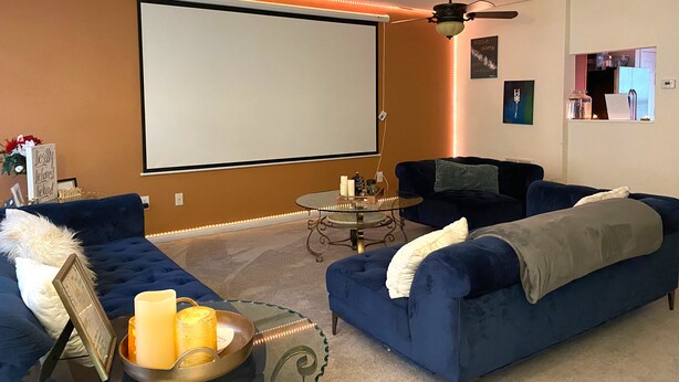 Una sala de estar con una pantalla grande, dos sofás, una mesa de centro y un ventilador de techo.