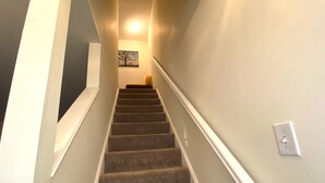 Una escalera con alfombra, barandillas blancas, un interruptor de luz y un cuadro en la pared.