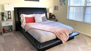 Un dormitorio con cama, mesitas de noche, una ventana con persianas y decoración en la pared.