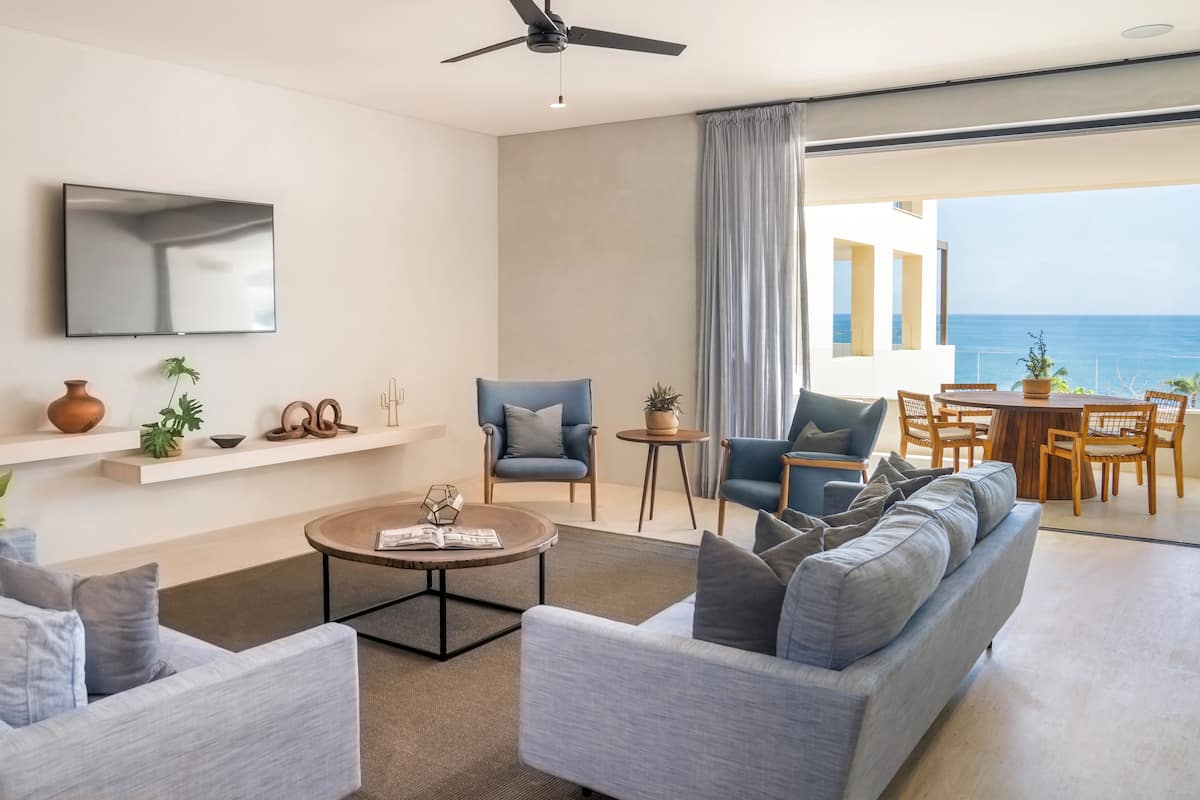 A modern living room with a sofa set, a coffee table, a TV, and a balcony with a view of the sea.