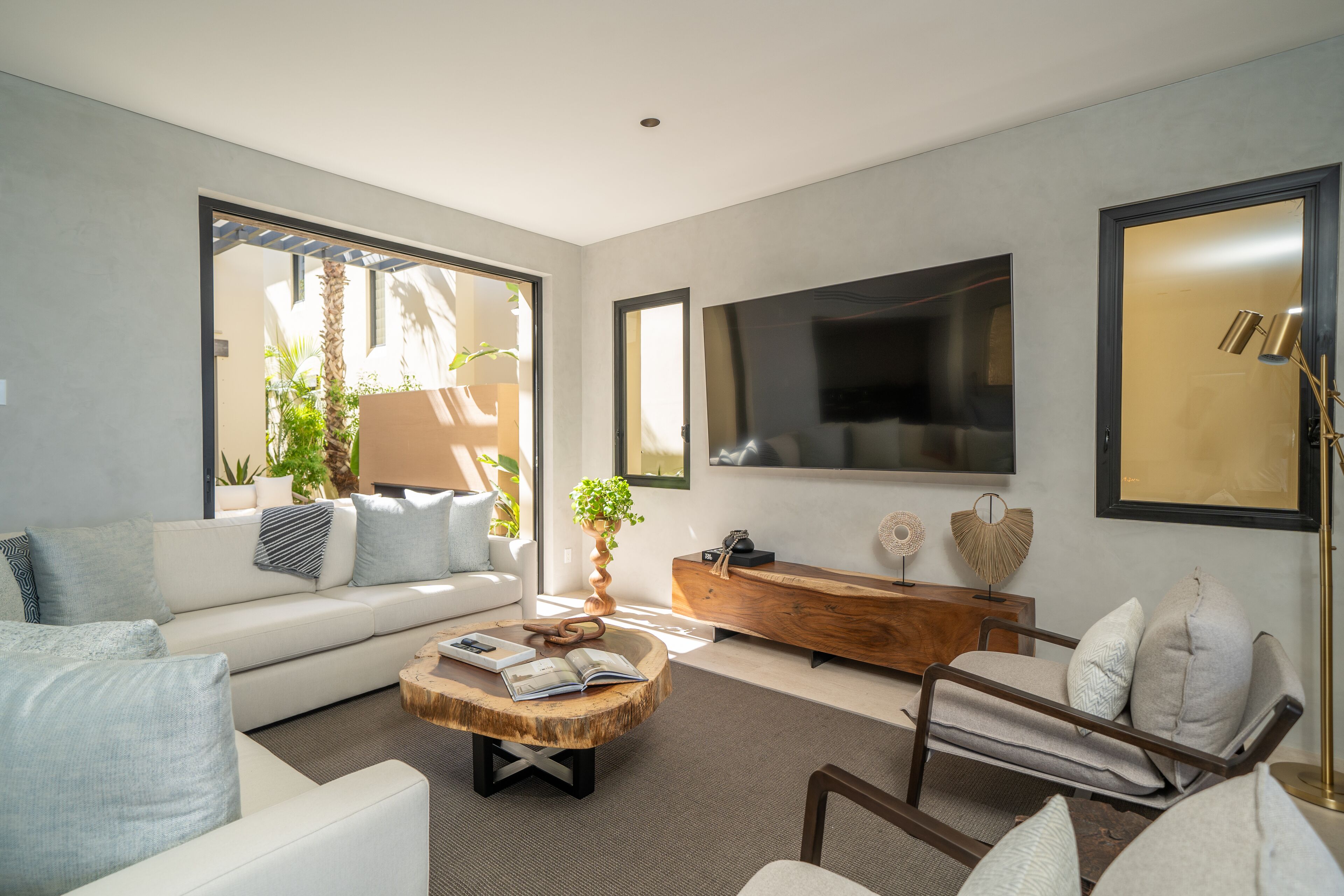 Una sala de estar moderna con un sofá, una mesa de centro y un sillón, una consola de madera y un televisor montado en la pared.