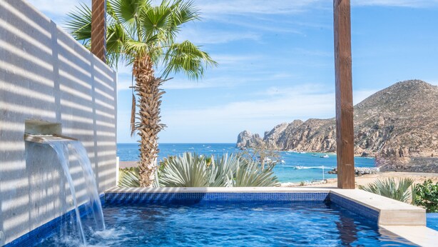Una piscina con cascada, palmeras y vistas al mar y a las montañas.