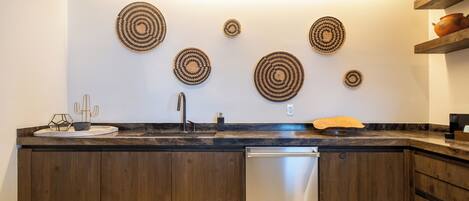 A modern kitchen with wooden cabinets, a stainless steel dishwasher, and decorative woven wall art.