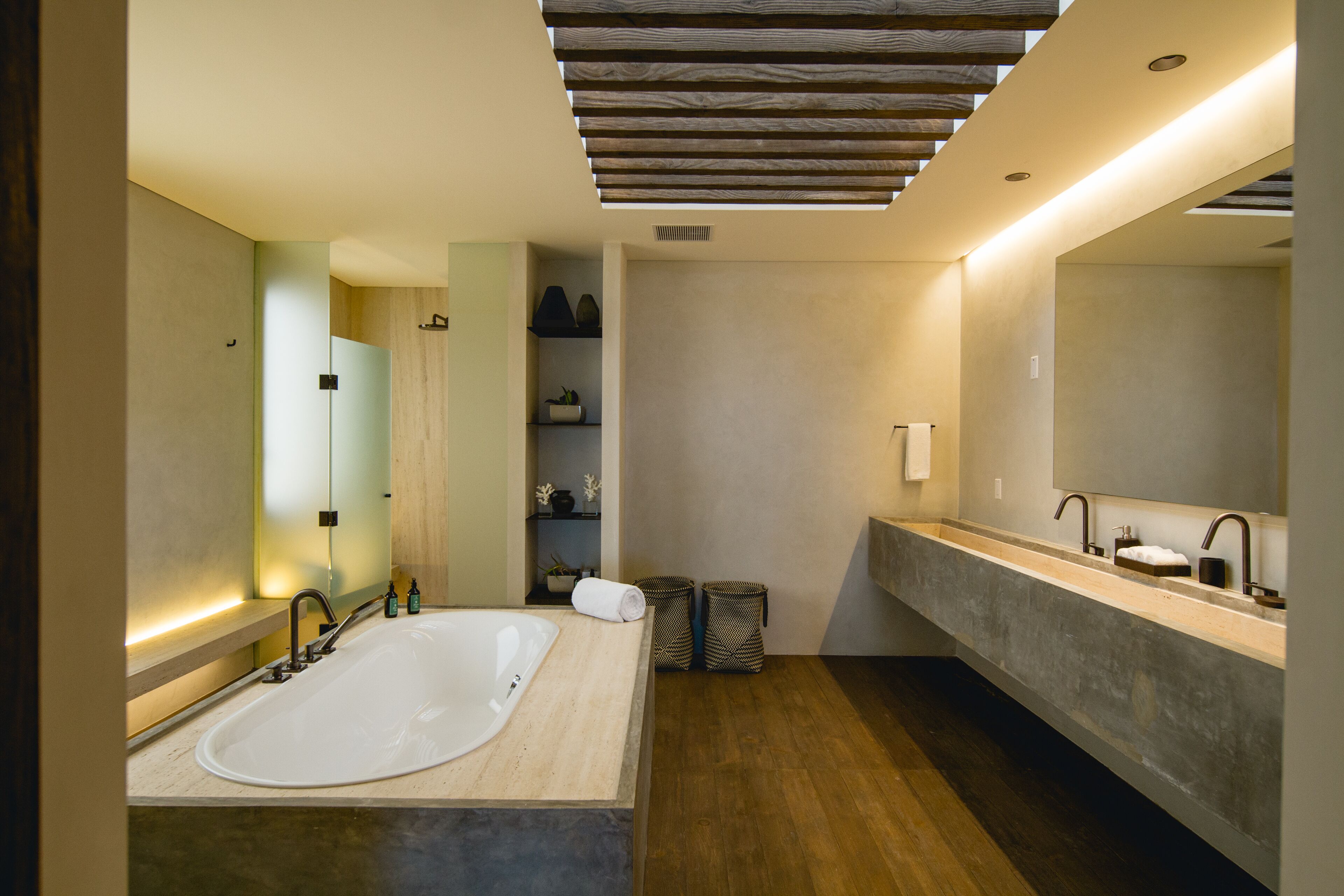 A modern bathroom with a large freestanding bathtub, a double vanity with a large mirror, and a wooden ceiling.