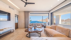 Una sala de estar moderna con un ventanal grande, un ventilador de techo y vista al mar.