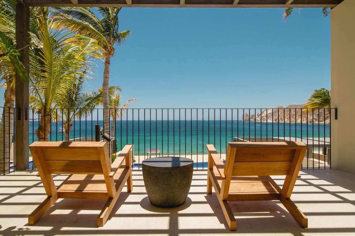 A balcony with two wooden chairs, a round table, and a view of the ocean.