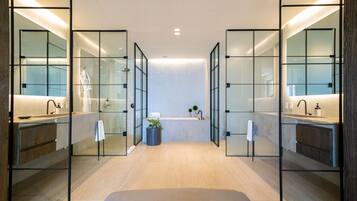 A modern bathroom with glass partitions, a central sink, and a plant.