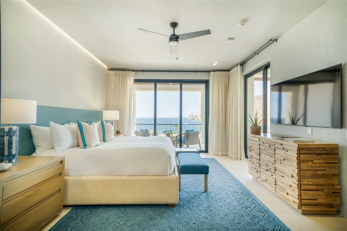 A modern hotel room with a large bed, a TV, a balcony with a view, and a wooden dresser.