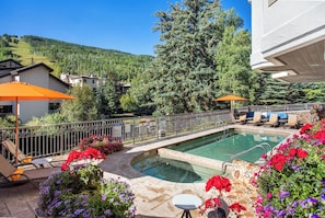 A swimming pool with a view of a forested hill, surrounded by lounge chairs and umbrellas.