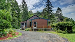 A cabin with a wooden exterior, a porch, and a gravel driveway.