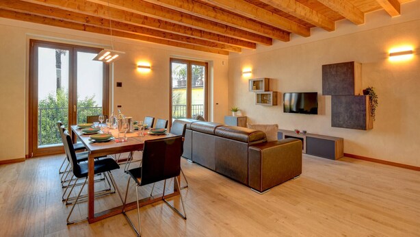 Ein geräumiges Zimmer mit Holzboden, einem Essbereich mit Tisch und Stühlen, einer Couch und einem an der Wand befestigten Fernseher.