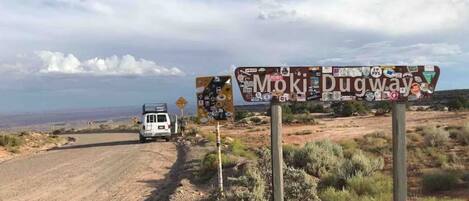A dirt road with a sign reading "Moki Dugway" and a white van parked on the side.