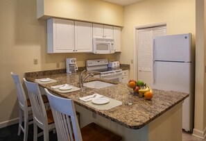 Compact kitchen with oven, microwave, and refrigerator, and a dining area for two.