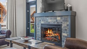 Una sala de estar moderna con chimenea de piedra, un televisor de pantalla plana montado encima y mobiliario de cuero.