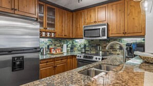 Una cocina con armarios de madera, un refrigerador de acero inoxidable, un microondas, una estufa y encimeras de granito.