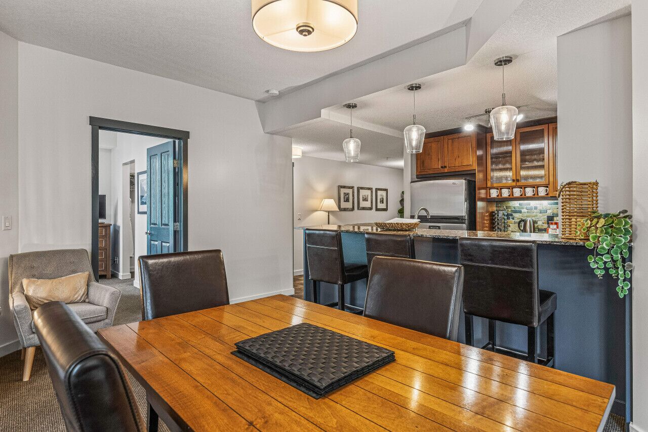 A modern dining area with a wooden table, black cushioned chairs, and pendant lighting.