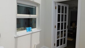 A room with a white door, a window with a blue decorative item, and a white wall. - The Annexe on Morris Street -  an annexe that sleeps 3 guests  in 2 bedrooms (Sheringham)