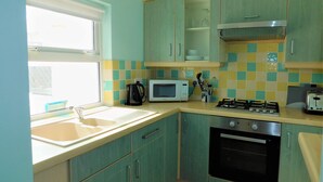 A kitchen with teal cabinets, a microwave, a gas stove, and a sink. - The Annexe on Morris Street -  an annexe that sleeps 3 guests  in 2 bedrooms (Sheringham)
