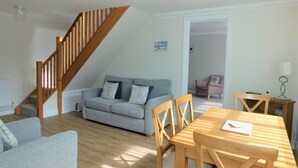 A cozy living room with a wooden staircase, a grey sofa, a wooden dining table with chairs, and a small table with a lamp. - The Annexe on Morris Street -  an annexe that sleeps 3 guests  in 2 bedrooms (Sheringham)