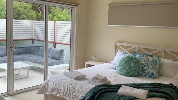 A bedroom with a bed, a nightstand, a window with a view of a patio area. - Contemporary On Cuttriss - Inlet Side (Inverloch)