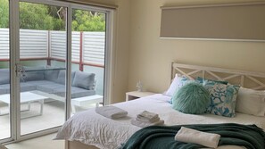 A bedroom with a bed, a nightstand, a window with a view of a patio area. - Contemporary On Cuttriss - Inlet Side (Inverloch)