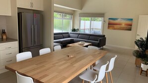 A modern kitchen with a wooden dining table, white chairs, a gray sofa, and a large refrigerator. - Contemporary On Cuttriss - Inlet Side (Inverloch)