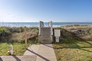 A wooden staircase leading to a beach with a sign indicating beach access.