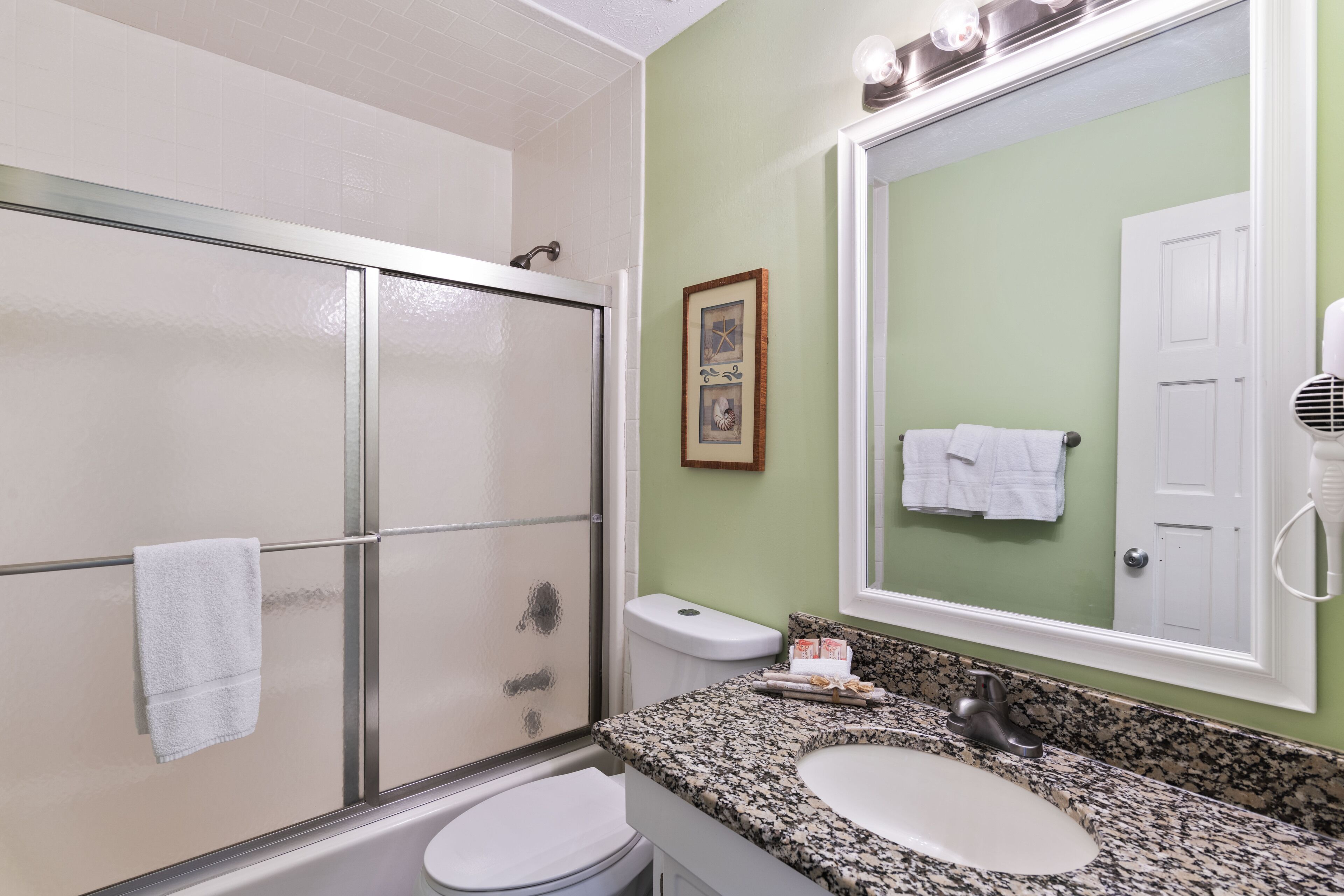 A bathroom with a glass shower door, a white toilet, a granite countertop sink, and a large mirror.