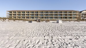 Un hotel de varios pisos con fachada simétrica, balcones y una playa arenosa al frente.