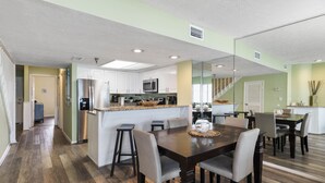 Una cocina moderna con armarios blancos, un refrigerador de acero inoxidable y un microondas. Hay un comedor con una mesa y sillas de madera.