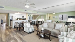 Amplia sala de estar con un sofá, sillones y una mesa de centro. Cuenta con una zona de cocina con armarios y una mesa de comedor.