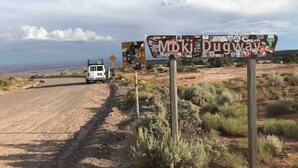 A dirt road with a sign reading "Moki Dugway" and a white van parked on the side.