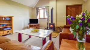 A cozy living room with a fireplace, a television, a bookshelf, and a coffee table. - Cider House at Oosland Barns - sleeps 4 guests  in 2 bedrooms (Bidford-on-Avon)