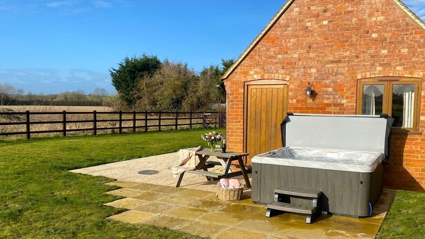 A brick building with a hot tub, a wooden door, and a small table with a vase of flowers. - Cider House at Oosland Barns - sleeps 4 guests  in 2 bedrooms (Bidford-on-Avon)