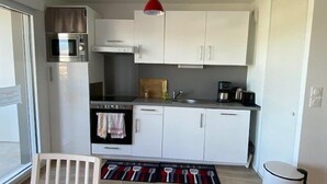 A compact kitchen with white cabinets, a stainless steel oven, a microwave, and a red pendant light. - Nice apartment 4 people in Hennebont wifi -  near Lorient 3 stars (HENNEBONT)