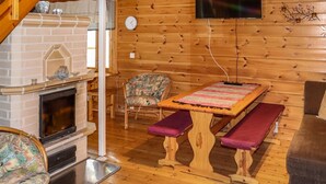 L’intérieur d’un chalet accueillant, avec une cheminée, des murs en bois, un téléviseur et un banc.