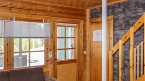 L’intérieur d’un chalet en bois, avec un canapé, une porte donnant sur l’extérieur et un escalier.