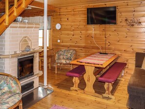 Interior acogedor de una cabaña con chimenea, paredes de madera, un televisor montado en la pared y un banco.