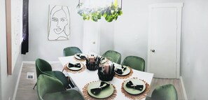 Un comedor con una mesa blanca dispuesta para seis personas, sillas verdes y una lámpara de araña moderna.