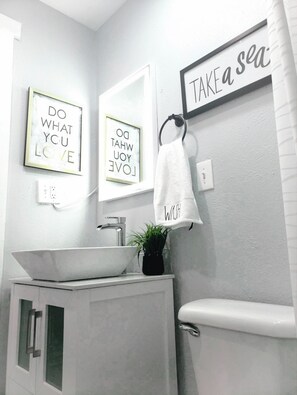 Un baño moderno con un lavabo blanco, un espejo y un cuadro con mensajes inspiradores.