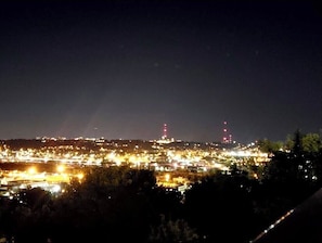 Vista nocturna de un paisaje urbano con edificios iluminados y torres rojas a lo lejos.