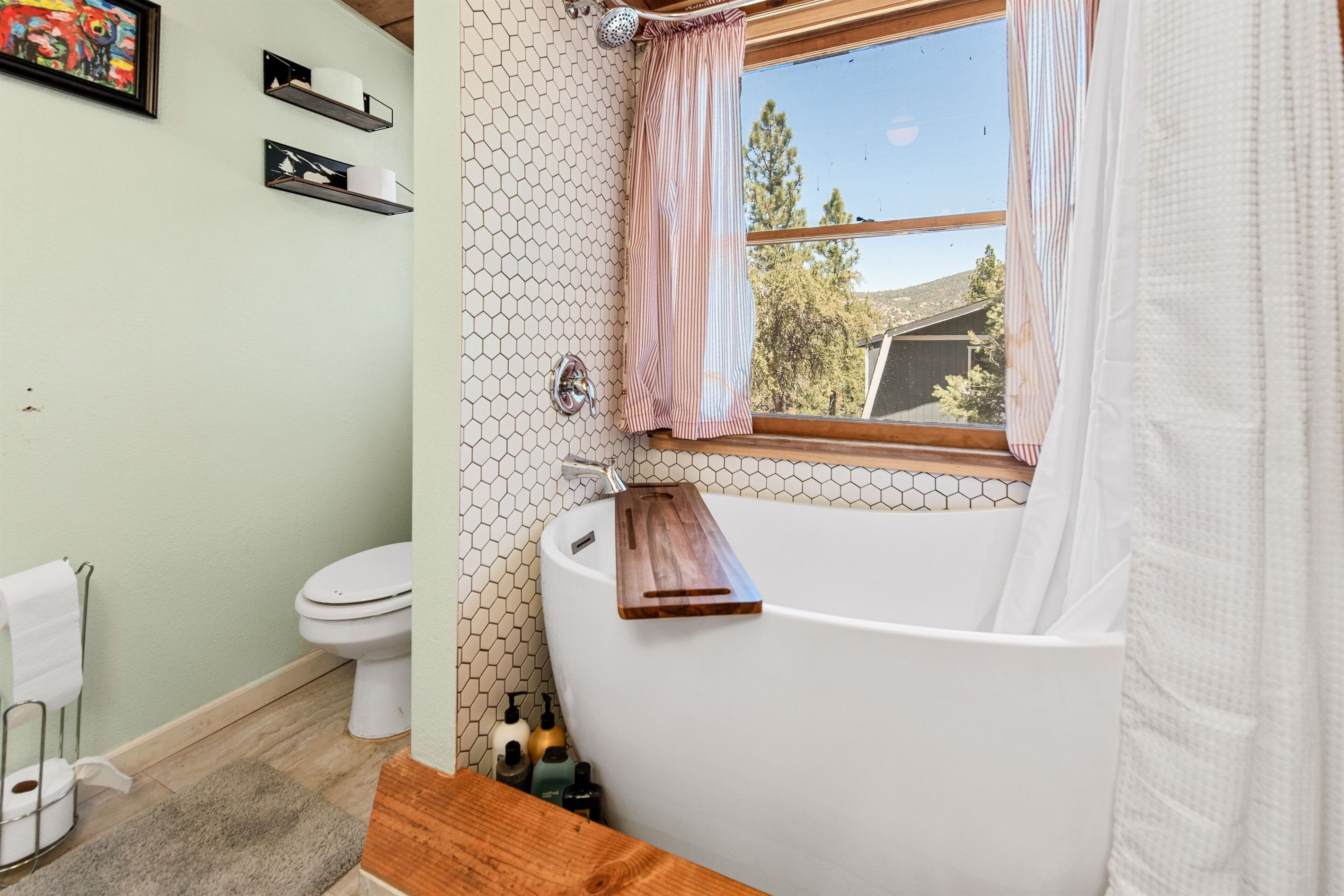 Un bagno con una vasca da bagno freestanding, un water e una finestra con vista su alberi e una casa.