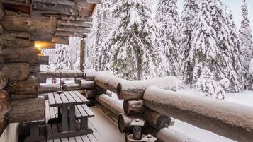 A wooden cabin with a snow-covered deck, a picnic table, and lanterns.