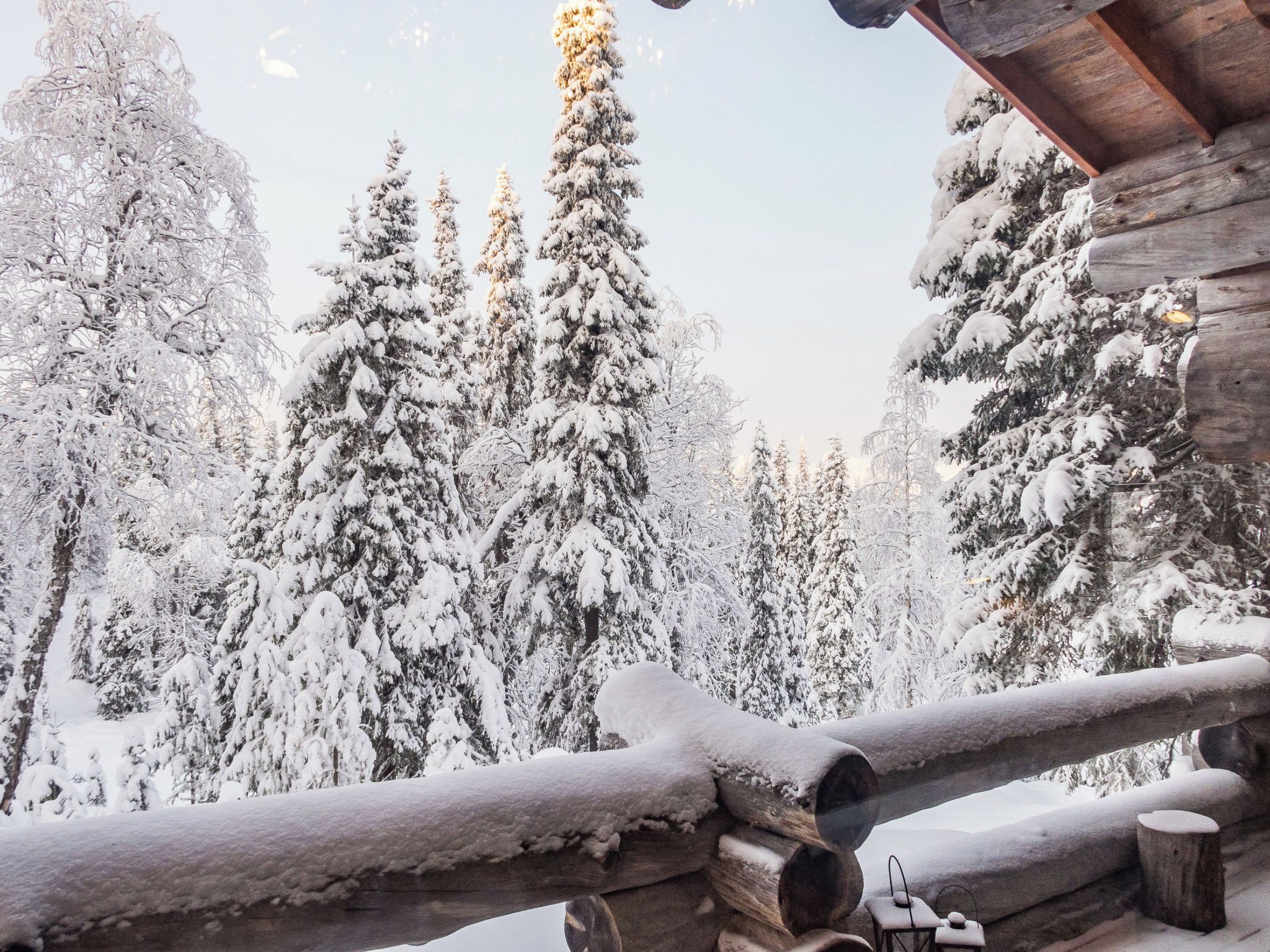 Una cabaña de troncos con el exterior cubierto de nieve, rodeada de árboles cargados de nieve.